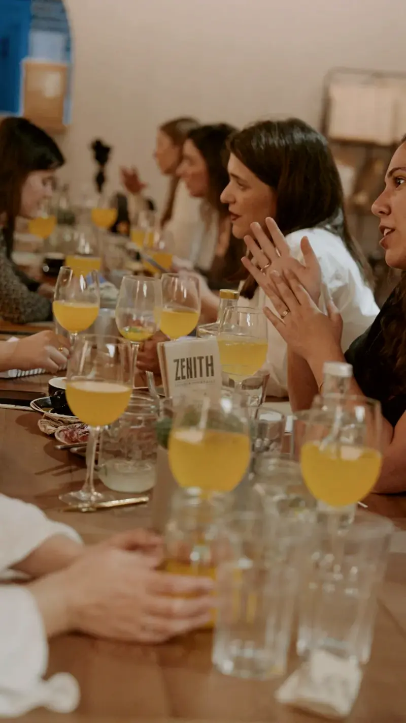 Duas mulheres em conversa à mesa, uma a gesticular com as mãos.